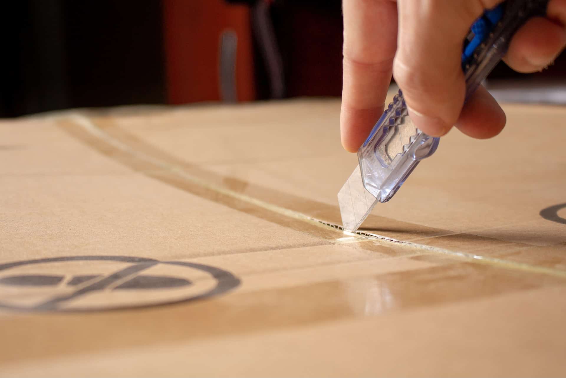 Close-up of a hand using a precision cutter on cardboard packaging.